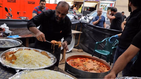 A man serves hot rice and stew to pilgrims during Arbaeen, offering free votive food.